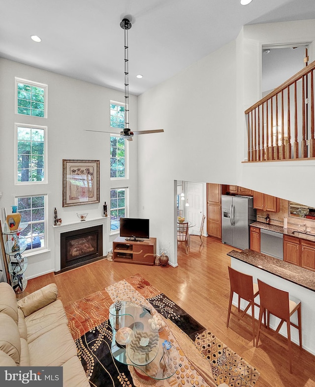 living area featuring a high ceiling, light wood-style floors, healthy amount of natural light, a glass covered fireplace, and recessed lighting