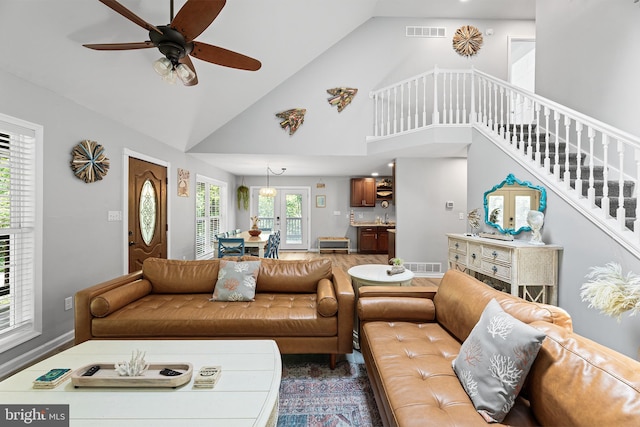 living area featuring stairs, a ceiling fan, and high vaulted ceiling