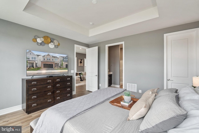bedroom featuring a tray ceiling, light wood-style floors, and baseboards