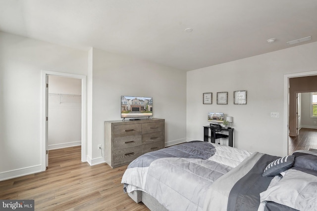 bedroom with wood finished floors, a walk in closet, and baseboards