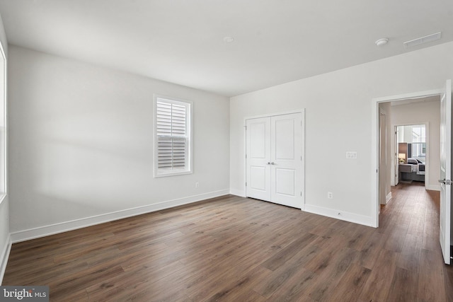 unfurnished bedroom featuring multiple windows, dark wood-style flooring, baseboards, and a closet