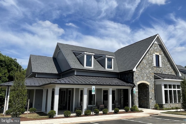 view of front facade featuring a standing seam roof, covered porch, a shingled roof, and stone siding