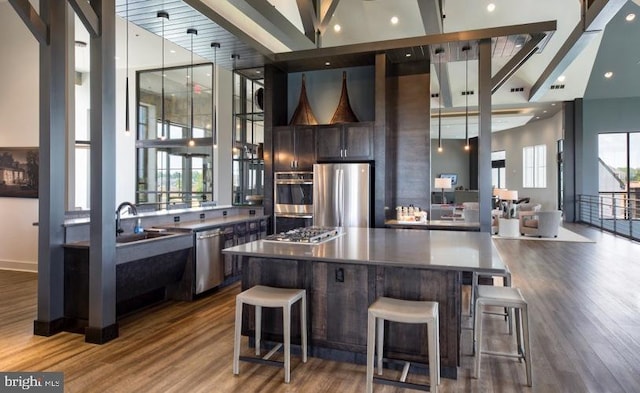 kitchen with appliances with stainless steel finishes, a towering ceiling, dark wood-style flooring, a sink, and a large island