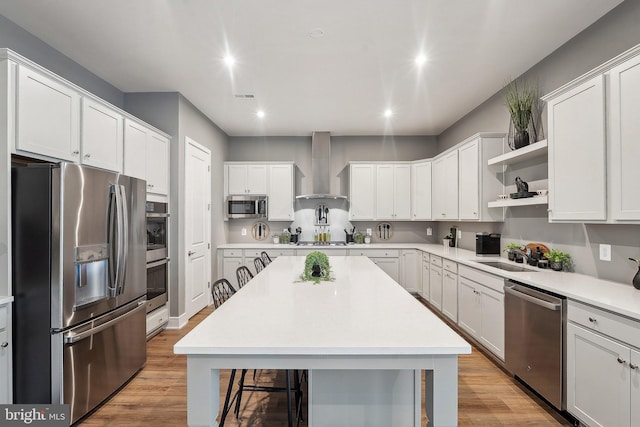 kitchen featuring stainless steel appliances, wall chimney exhaust hood, a kitchen bar, a sink, and open shelves