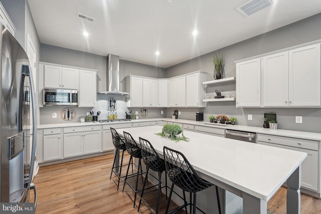 kitchen featuring wall chimney exhaust hood, appliances with stainless steel finishes, a breakfast bar, light countertops, and a sink