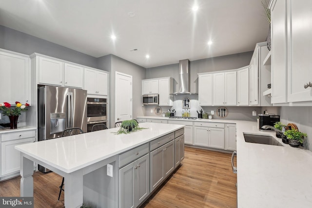 kitchen featuring wall chimney range hood, a sink, gray cabinets, appliances with stainless steel finishes, and a kitchen island