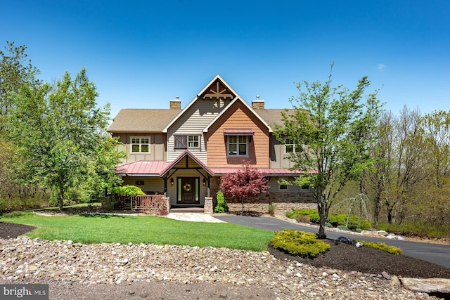 view of front of house featuring a chimney, stone siding, a front yard, and a standing seam roof