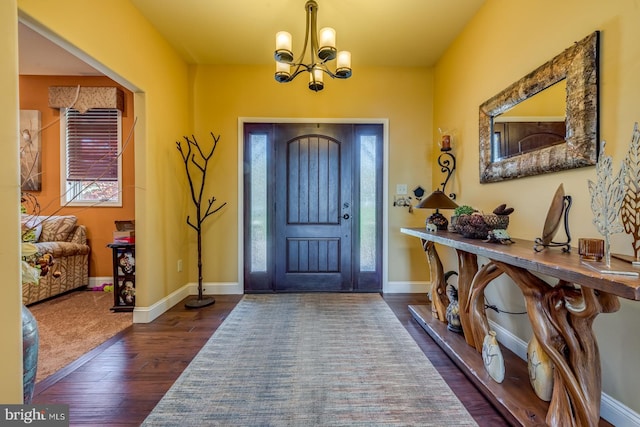 foyer entrance with dark wood-type flooring, a chandelier, and baseboards