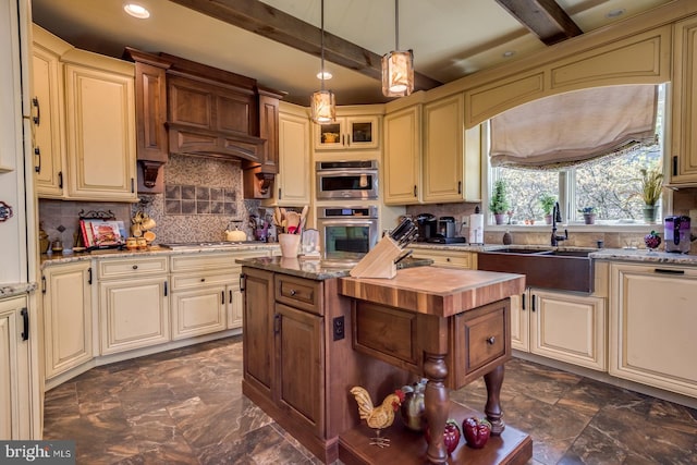 kitchen featuring cream cabinetry, beamed ceiling, a sink, backsplash, and light stone counters