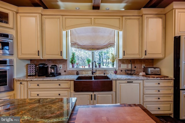 kitchen with cream cabinetry, a sink, stainless steel oven, and backsplash
