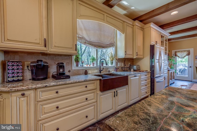 kitchen featuring cream cabinets, high quality fridge, a sink, backsplash, and beamed ceiling