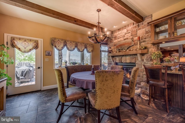 dining room featuring beamed ceiling, stone tile floors, a chandelier, baseboards, and a stone fireplace