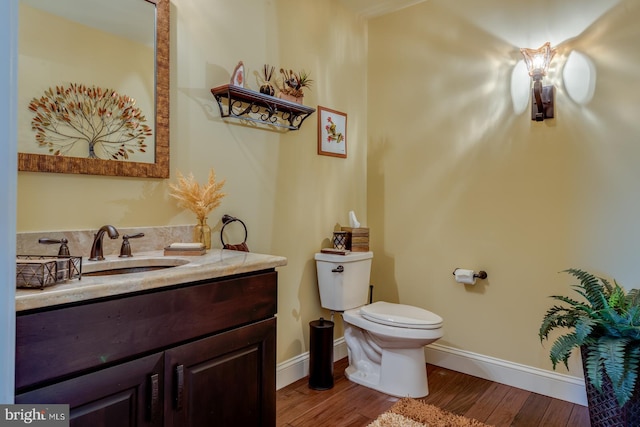 half bath with toilet, baseboards, wood finished floors, and vanity