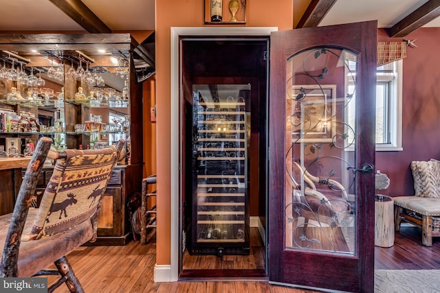 wine cellar with beamed ceiling, beverage cooler, a bar, and wood finished floors