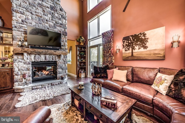 living room with a stone fireplace, wood finished floors, a towering ceiling, and baseboards
