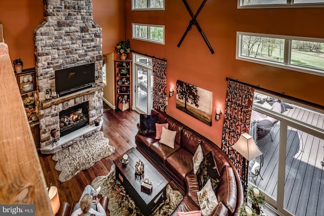 living room featuring a stone fireplace, a towering ceiling, and wood finished floors