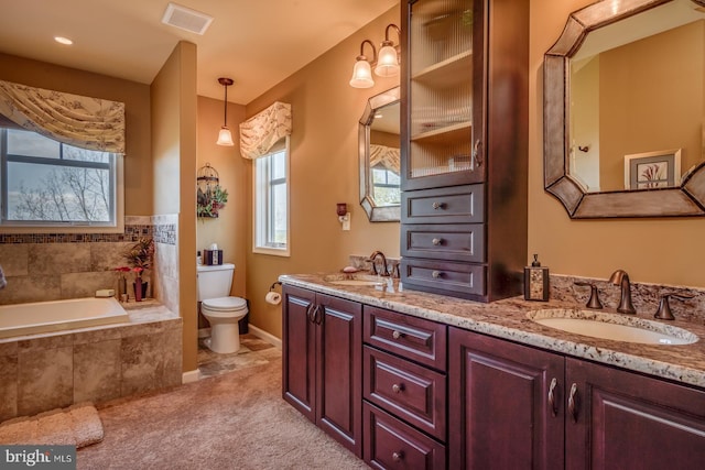 full bathroom with toilet, double vanity, tiled bath, and baseboards