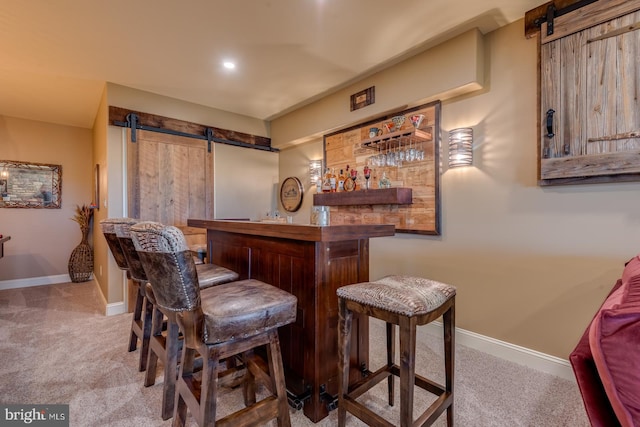 indoor dry bar with a barn door, carpet, and baseboards