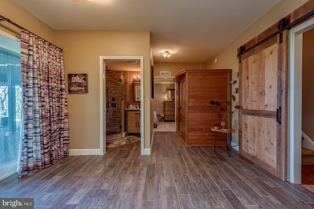 unfurnished bedroom with dark wood finished floors, a barn door, and baseboards