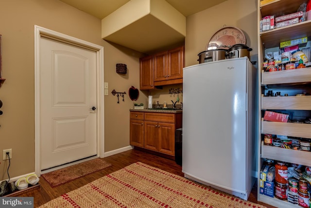 kitchen with freestanding refrigerator, dark wood finished floors, brown cabinets, a sink, and baseboards