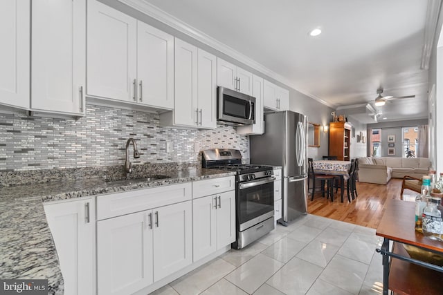 kitchen featuring appliances with stainless steel finishes, a sink, crown molding, backsplash, and stone counters
