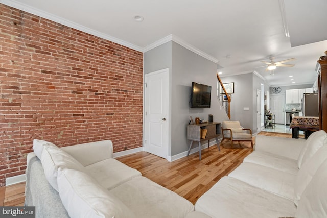 living area featuring baseboards, stairway, brick wall, light wood-style flooring, and ceiling fan