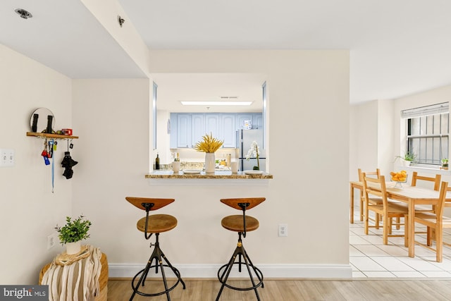 bar area featuring stainless steel fridge, light wood finished floors, and baseboards