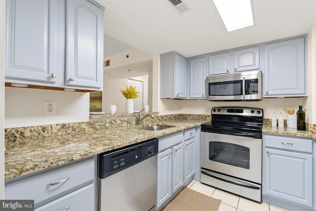 kitchen with stainless steel appliances, a sink, light tile patterned floors, and light stone countertops