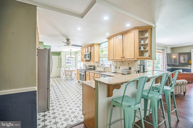 kitchen featuring stainless steel appliances, a sink, a peninsula, crown molding, and light brown cabinetry