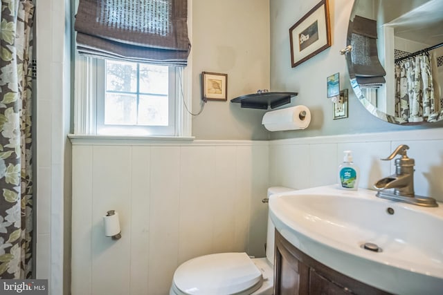 bathroom with toilet, a wainscoted wall, a shower with curtain, a decorative wall, and vanity