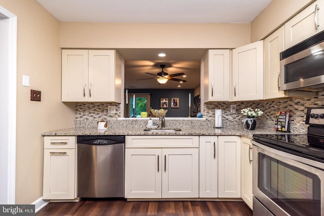 kitchen featuring appliances with stainless steel finishes, a sink, ceiling fan, dark wood finished floors, and light stone countertops