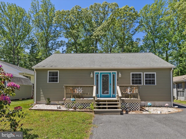 view of front of home with a deck, a front lawn, and roof with shingles
