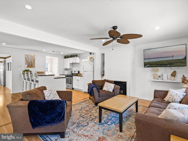 living room with light wood-style flooring, a ceiling fan, baseboards, a fireplace, and recessed lighting