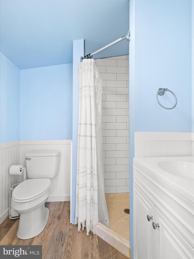 bathroom featuring wainscoting, a stall shower, toilet, wood finished floors, and vanity