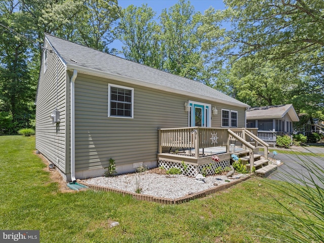 rear view of house with a wooden deck, a yard, and a shingled roof
