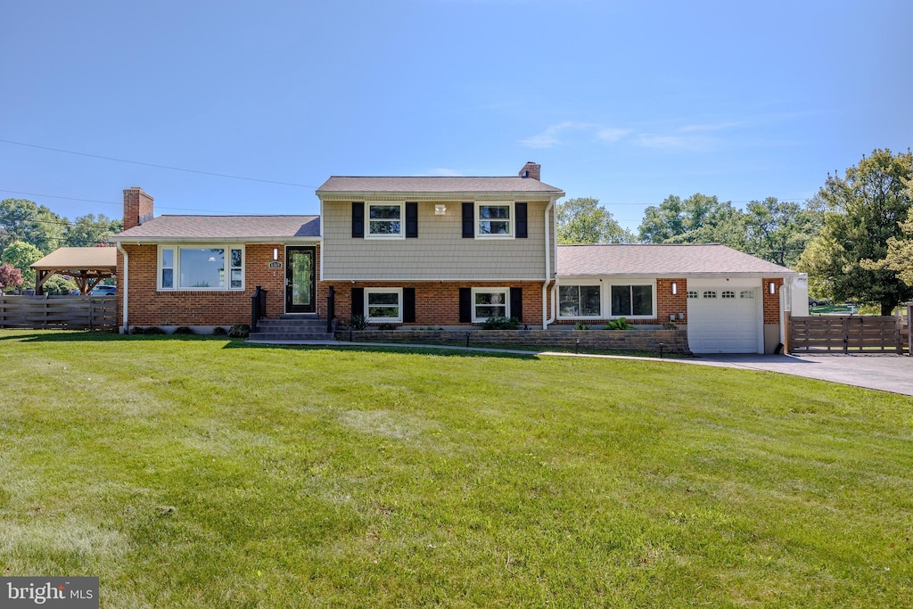 tri-level home with a garage, a chimney, brick siding, concrete driveway, and a gazebo