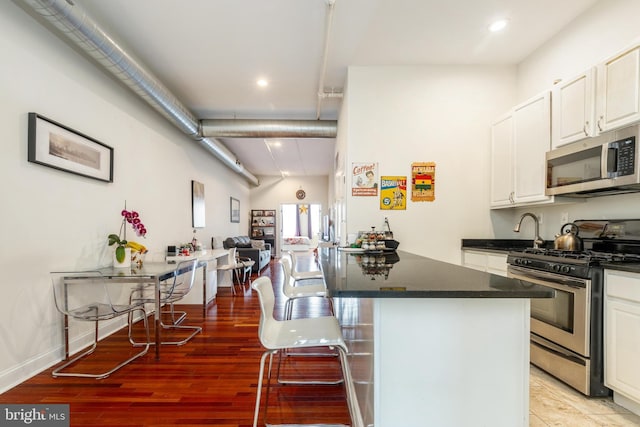 kitchen with appliances with stainless steel finishes, dark countertops, white cabinetry, a kitchen breakfast bar, and light wood-type flooring