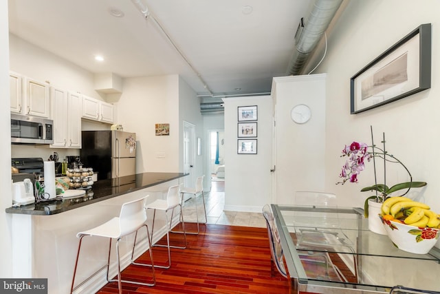 kitchen with stainless steel appliances, a kitchen bar, dark countertops, light wood finished floors, and white cabinets