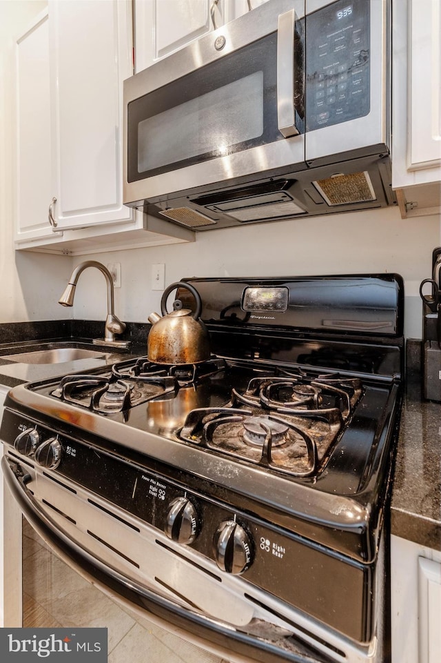 kitchen featuring black gas stove, stainless steel microwave, white cabinetry, and dark countertops
