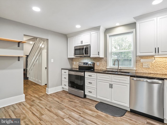 kitchen featuring appliances with stainless steel finishes, a sink, white cabinetry, backsplash, and baseboards