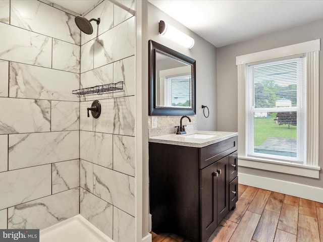 bathroom with tiled shower, vanity, wood finished floors, and baseboards