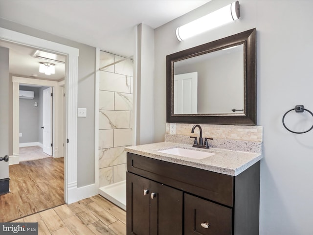 bathroom featuring an AC wall unit, wood finished floors, tiled shower, vanity, and tasteful backsplash