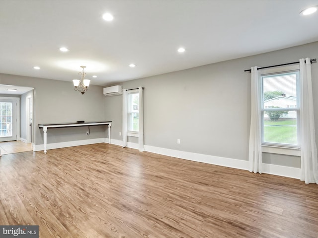 unfurnished living room with a wall unit AC, a chandelier, recessed lighting, and light wood-style floors