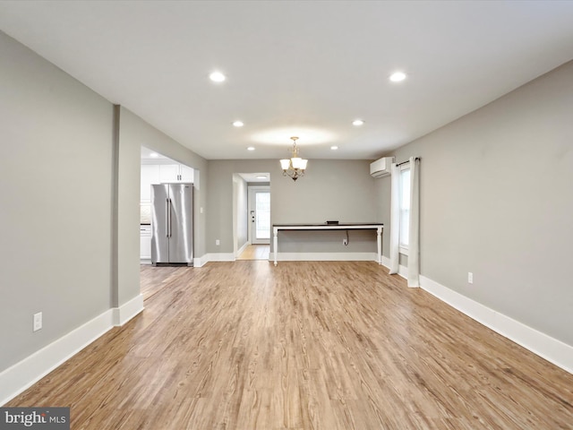 unfurnished living room featuring a wall unit AC, a chandelier, recessed lighting, light wood-style flooring, and baseboards