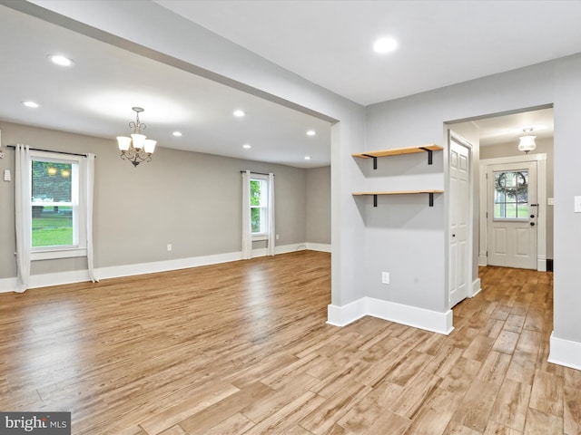 unfurnished living room featuring light wood finished floors, a chandelier, baseboards, and recessed lighting
