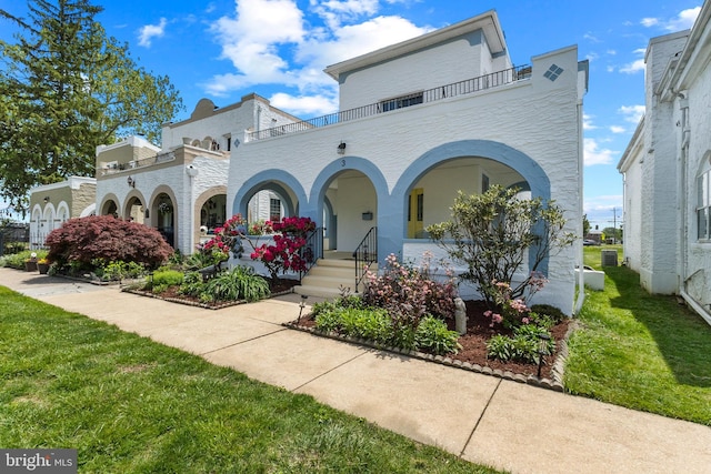 view of front of home with a balcony, a front lawn, and stucco siding