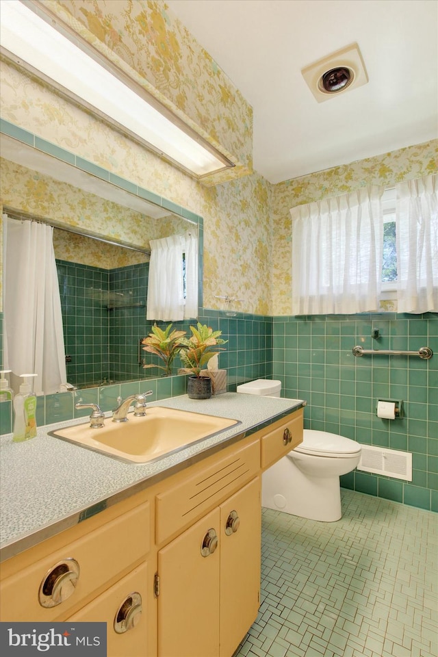 full bathroom with wallpapered walls, tile walls, toilet, wainscoting, and vanity