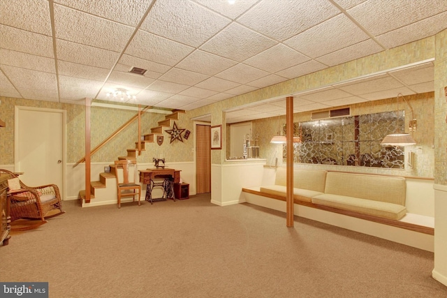 finished below grade area with stairway, wallpapered walls, carpet floors, and a paneled ceiling