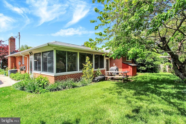 rear view of property with brick siding, a sunroom, a chimney, and a yard