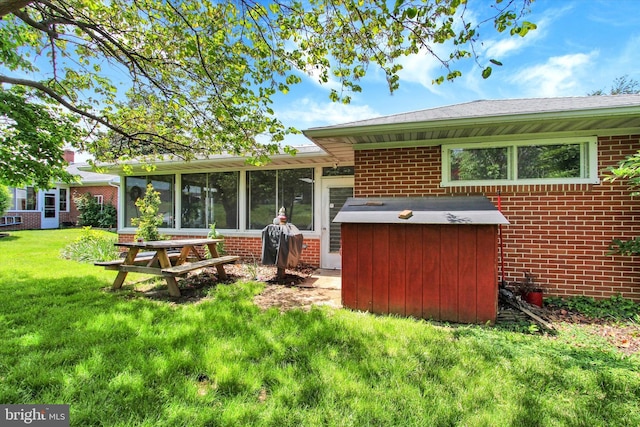 back of house featuring brick siding, a sunroom, and a lawn